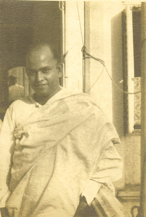 Asit Krishna Mukherji in a white shawl, smiling, standing by a window