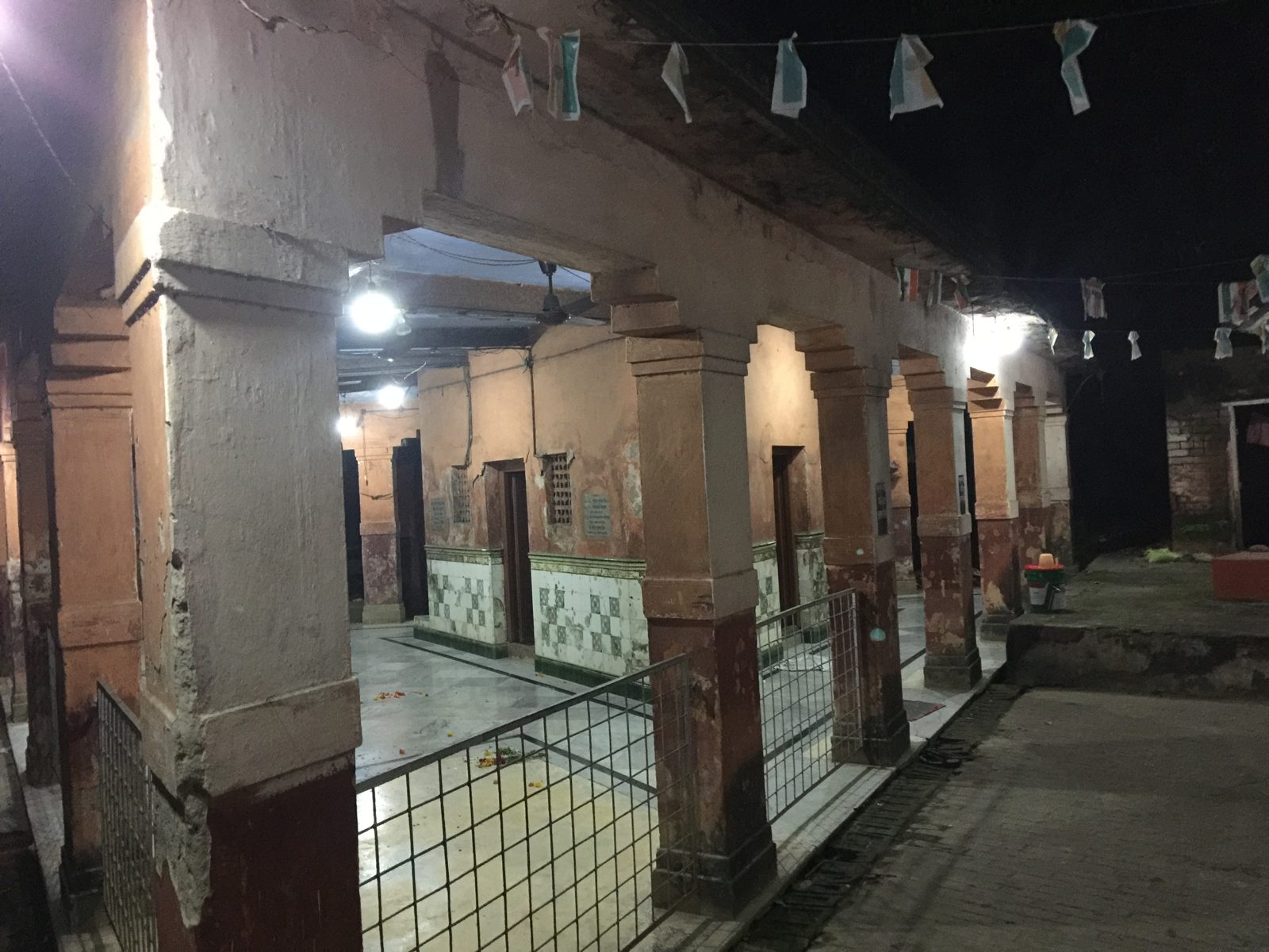 A long pillared hall at night with chequered tiles and paper flags strung across the courtyard